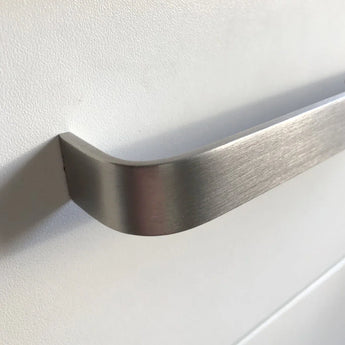 Gros plan d'une poignée Leonardo Stainless Steel Deluxe de yessential.fr en aluminium brossé, montée sur une façade d'armoire ou de tiroir blanc lisse, avec un éclairage doux projetant une ombre sur la surface.