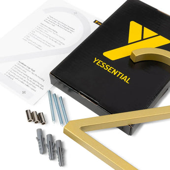 Une boîte noire yessential.fr avec un logo jaune est présentée avec des supports métalliques Amato Gold de 12,5 cm, des vis, des chevilles murales et des instructions (idéales pour monter des numéros de maison élégants) sur un fond blanc.