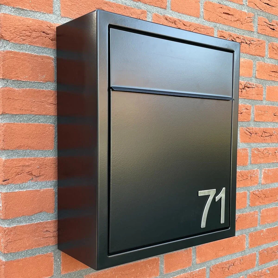 Une boîte aux lettres en métal noir portant le numéro 71, avec les numéros Animo en acier inoxydable de 5 cm (sans perçage) yessential.fr, est montée sur un mur de briques rouges.