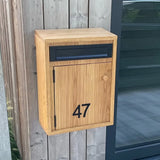 Une boîte aux lettres en bois avec une boîte aux lettres noire et le numéro 47, utilisant Animo Black 7 (6 cm, sans perçage) de yessential.fr, est montée sur un mur en bois à côté d'une porte vitrée.