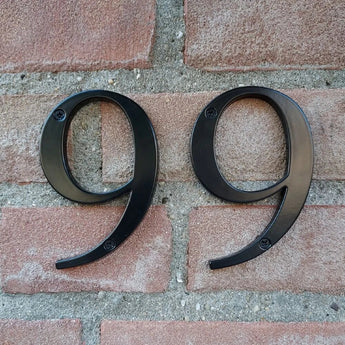 Deux numéros Matteo Black 10 cm de yessential.fr, tous deux neufs, sont montés côte à côte sur un mur de briques rouges. Ils sont chacun fixés avec deux vis pour une apparence élégante.