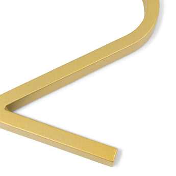 Un gros plan du numéro de maison Amato Gold de 12,5 cm de yessential.fr, présentant un motif doré métallique fortement incurvé en forme de V partiel ou de losange sur fond blanc.