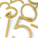 Les chiffres métalliques Amato Gold de 12,5 cm de yessential.fr sont disposés sur une surface blanche. Avec des lignes épurées et une finition lisse, certains se chevauchent dans un coin, donnant à toute entrée un look moderne et élégant.