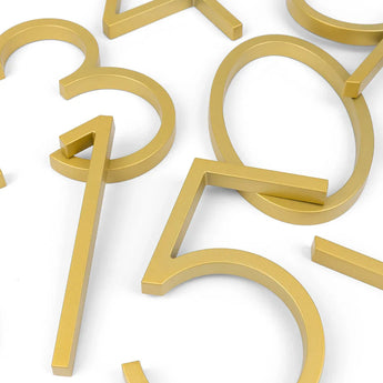 Les numéros de maison Amato Gold 15 cm de yessential.fr (0, 1, 3, 4, 5 et 7) sont de couleur dorée et forment ensemble une composition moderne et ludique sur fond blanc grâce à leur placement superposé.