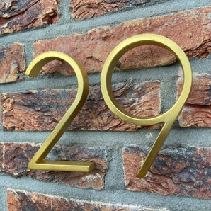 Les numéros de maison Amato Gold 12,5 cm de yessential.fr sont montés sur un mur de briques avec du mortier gris pour un look moderne.