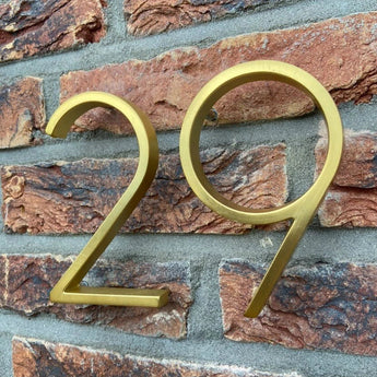 Les numéros de maison Amato Gold 12,5 cm de yessential.fr sont montés sur un mur de briques avec du mortier gris pour un look moderne.