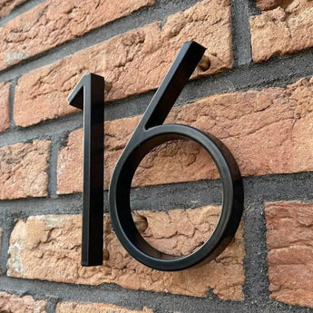 Les numéros de maison Amato Black 12,5 cm de yessential.fr sont montés sur des murs en briques rouges et légèrement éloignés pour projeter une ombre subtile pour un look noir moderne.