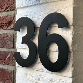 L'Adamo Black 20cm de yessential.fr, avec le numéro « 36 » en noir sur un mur de briques blanches avec des briques rouges à gauche, est un exemple élégant de numéros de maison modernes.
