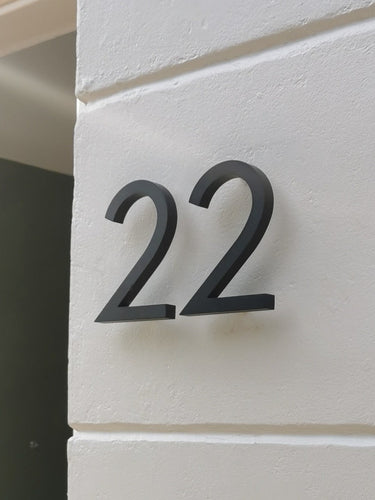 Le numéro de maison Milano Black 10 cm de yessential.fr présente un élégant « 22 » noir sur un mur blanc lisse. Fabriqué en aluminium, il crée des ombres douces, rendant ce numéro de maison à la fois fonctionnel et élégant.