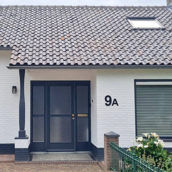 Une maison avec une fenêtre et une porte, équipée d'un numéro de maison Animo Noir 20 cm (sans perçage) pour une pose facile et autocollante.