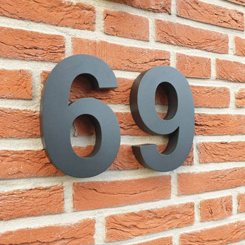 Les Angelo Black 20cm de yessential.fr sont de grands numéros de maison 3D noirs, montés sur un mur de briques rouges avec des joints visibles et une texture rustique, idéaux comme numéros de maison modernes.