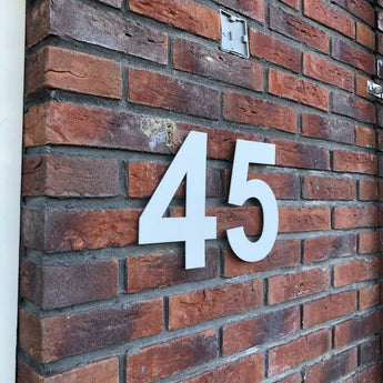 Le numéro de maison Adamo White 15 cm de yessential.fr se démarque des murs en briques et allie style moderne et haute visibilité pour un impact maximal.