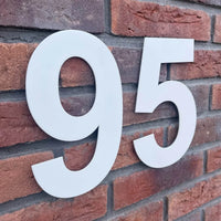 Le numéro de maison 95 Adamo White 20 cm de yessential.fr se détache magnifiquement sur un mur de briques rouges, rendant les numéros de bâtiment ou de maison clairement visibles.