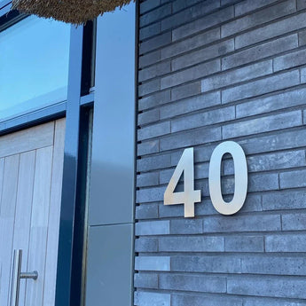 L'extérieur d'un bâtiment moderne présente des murs en briques grises, une porte en bois avec une poignée en métal et un grand numéro de maison de 8 pouces fixé au mur.