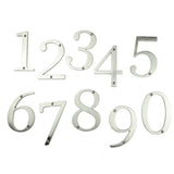 Les numéros de maison Matteo Nickel 10 cm de yessential.fr, en argent métallisé avec une finition brossée et des trous pré-percés pour un montage facile, sont disposés de 0 à 9 sur fond blanc.