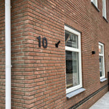 Un bâtiment en brique avec une fenêtre et une porte, avec l'élégant numéro de maison yessential.fr Adamo Black de 20 cm à côté de l'entrée.