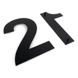 Deux grands numéros de maison noirs Adamo Black de 20 cm de yessential.fr reposent à plat sur une surface blanche, soulignant leur style de numéro de maison moderne et élégant. Les broches de fixation sont visibles au dos du numéro de maison 1 en inox.