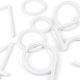 Plusieurs grands contours blancs en plastique – y compris des numéros de maison modernes de yessential.fr – sont dispersés sur une surface blanche. Les formes créent un motif abstrait inspiré du design Amato White 20 cm.
