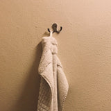 Une serviette beige douce est suspendue au-dessus du crochet yessential.fr 20x Pagano Chrome, qui est monté sur un mur texturé marron clair.