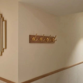 Le porte-manteau Eduardo Gold Deluxe de yessential.fr, avec cinq crochets dorés, est monté sur un mur de couloir clair avec finition en bois. Les photos encadrées à gauche ajoutent de l'élégance à cet écran élégant de yessential.fr.
