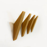Quatre crochets Fabio Beech de yessential.fr sont montés en diagonale sur un mur blanc en zigzag. Ces crochets en bois de hêtre ont un design minimaliste et géométrique et sont uniformément espacés.