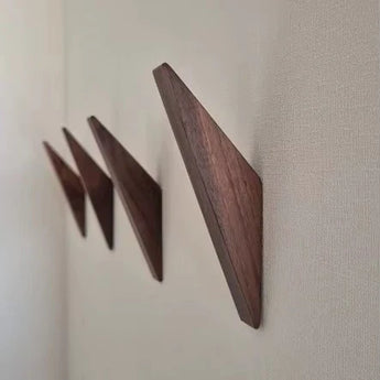Trois crochets Fabio Walnut de yessential.fr sont montés en rangée sur un mur de couleur claire, chacun étant incliné vers le haut pour former un porte-manteau en bois minimaliste à l'attrait géométrique.
