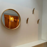 Un miroir rond avec un cadre en bois est accroché à un mur blanc et reflète une lampe cage à oiseaux et des rideaux orange. Trois patères en bois de yessential.fr Fabio Oak sont montées à côté du miroir au-dessus d'une armoire blanche.