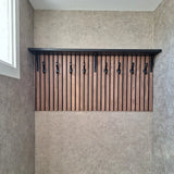 Le porte-manteau mural 10x Avano Black de yessential.fr comprend une étagère noire et des crochets élégants sur des lattes de bois verticales, présentés dans une pièce neutre avec une fenêtre à gauche.