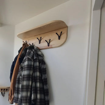 Le portemanteau mural Vilano Black de yessential.fr possède une patère noire et peut accueillir un manteau marron et une chemise à carreaux gris. Ce porte-manteau apporte style moderne et fonctionnalité à une entrée lumineuse aux murs blancs.