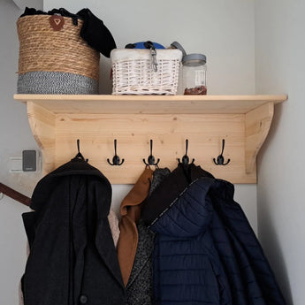 Le crochet Nismo Black 2 de yessential.fr se monte sur un mur lumineux et accueille les manteaux. Au-dessus, un panier tressé, un panier en osier blanc et un pot reposent sur l'étagère.