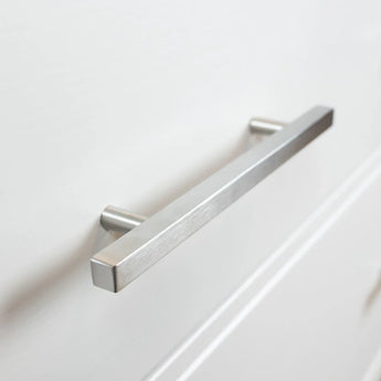 Un gros plan de la poignée en acier inoxydable, montée sur une porte d'armoire blanche. Cette poignée rectangulaire moderne présente un design minimaliste élégant avec une finition en acier inoxydable brossé.