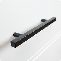 Un gros plan de la poignée Marano Black de yessential.fr, une poignée de tiroir rectangulaire noir mat moderne sur une façade blanche, qui accentue les poignées minimalistes pour un look élégant et contemporain.