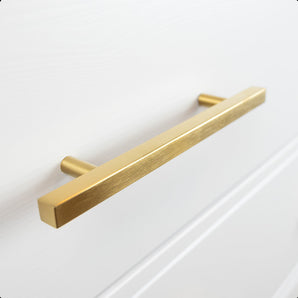 Un gros plan de la poignée rectangulaire Marano Gold de yessential.fr, élégamment montée sur une façade de meuble ou de tiroir blanche.