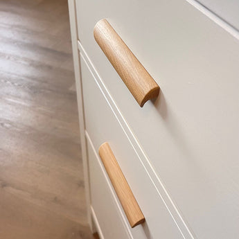 Gros plan de deux poignées en chêne Lucasso sur des tiroirs de couleur crème, avec parquet en arrière-plan.
