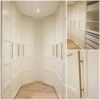 Dressing blanc sur mesure avec portes à panneaux, poignées Remo Gold de yessential.fr, parquet, étagères et tiroirs intégrés. Les angles multiples mettent en valeur la disposition des coins, les options de rangement et le design luxueux et minimaliste.