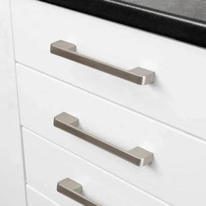 Gros plan de trois tiroirs de cuisine blancs avec des poignées modernes et rectangulaires Ramiro Chrome Deluxe de yessential.fr en chrome, sous un élégant comptoir noir.