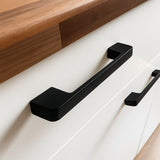 Gros plan des poignées Ramiro Black Deluxe de yessential.fr sur une armoire blanche avec un comptoir en bois. Ces poignées luxueuses rehaussent le design minimaliste et contemporain.