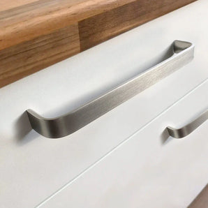 Gros plan d'un tiroir de cuisine moderne avec poignées Leonardo Stainless Steel Deluxe de yessential.fr sur une armoire blanche, avec un comptoir en bois sur le dessus.
