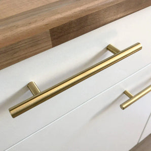 Gros plan d'une armoire de cuisine moderne à façade blanche, équipée de la poignée Remo Gold de yessential.fr. Un comptoir en bois au fini naturel apparaît en haut de l’image.