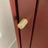 Un gros plan du bouton Remo Gold Deluxe de yessential.fr, un bouton de meuble de luxe en or avec un design cylindrique texturé, présenté sur une armoire ou un tiroir rouge foncé mat.