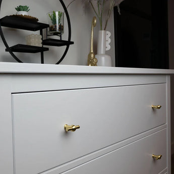 Un buffet blanc avec un bouton Rando Gold de yessential.fr et un design autour du design d'un ensemble de petites plantes et d'un décor. Les vases et la figure d'oiseau sont basés sur le design idéal pour un style intérieur moderne.