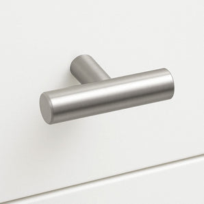 Un bouton Remo en acier inoxydable de yessential.fr, avec une forme en T en métal brossé et un design cylindrique mat, est monté sur un tiroir d'armoire blanc pour un look simple et moderne.