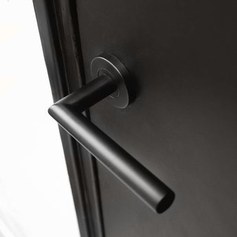 Un gros plan de la poignée de porte Lucio Black de yessential.fr, avec une poignée cylindrique noire mate montée horizontalement sur une porte sombre - un exemple élégant de poignées de porte noires modernes.