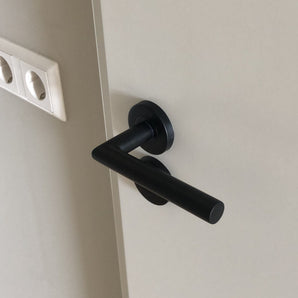 La serrure WC Rodi Black de yessential.fr, au design cylindrique épuré en noir mat, est montée sur une porte de couleur claire. Il y a deux prises blanches sur le mur à côté de la porte.