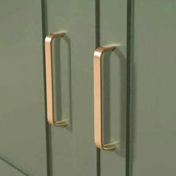 Gros plan des poignées Leonardo Gold Deluxe de yessential.fr sur des portes d'armoires vertes avec un design à rainure verticale, ajoutant un style de cuisine de luxe.