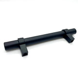 L'Arturo Black de yessential.fr est une tige métallique cylindrique noire avec deux supports de montage rectangulaires, chacun avec un trou de vis, qui souligne l'aspect élégant des poignées noires mates sur un fond blanc uni.