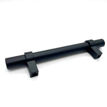 L'Arturo Black de yessential.fr est une tige métallique cylindrique noire avec deux supports de montage rectangulaires, chacun avec un trou de vis, qui souligne l'aspect élégant des poignées noires mates sur un fond blanc uni.