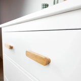 Gros plan sur le buffet Arriero Oak de yessential.fr, avec de grandes poignées minimalistes en chêne. Ce buffet blanc moderne présente quelques objets décoratifs sur le dessus.