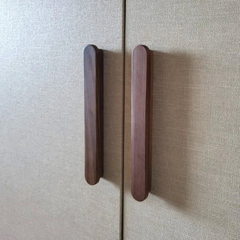 Deux poignées Arriero Walnut de yessential.fr sont fixées aux portes d'une armoire texturée beige, placées rapprochées le long de la couture où les deux portes se rejoignent.
