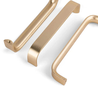 Trois poignées d'armoire Leonardo Gold Deluxe de yessential.fr, dans un design élégant et rectangulaire de couleur dorée, sont disposées sur un fond blanc – deux posées à plat et une inclinée pour montrer différentes perspectives.